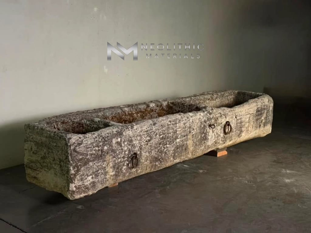 Trough FG103-19.95x22x16 high-angle perspective studio view showing the full length of a textured ancient limestone basin with weathered gray patina, dual rustic iron hardware rings, and thick divided interior compartments.