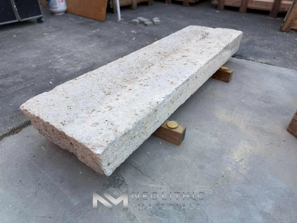 Slab FG103-59.79x23x8 high-angle side view showcasing the full length and heavily pitted surface details of a reclaimed rectangular limestone block elevated on small wood blocks.