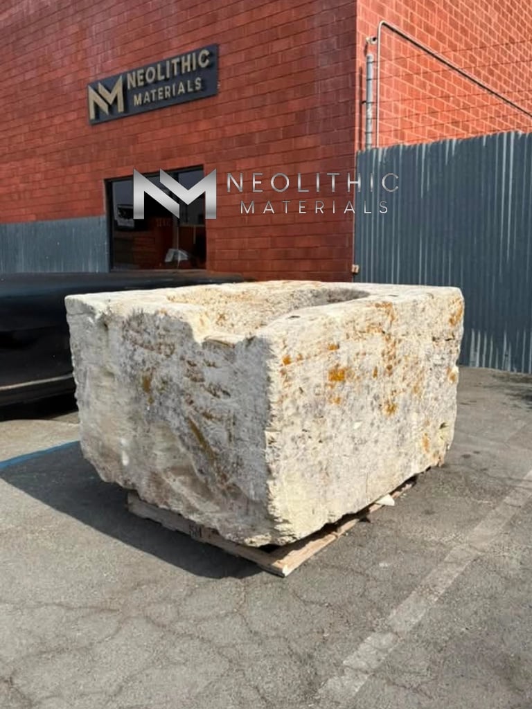 Trough FG104-25.57x53x35 massive block of antique limestone with natural yellow lichen growing on its chiseled exterior surface resting on a pallet outdoors.