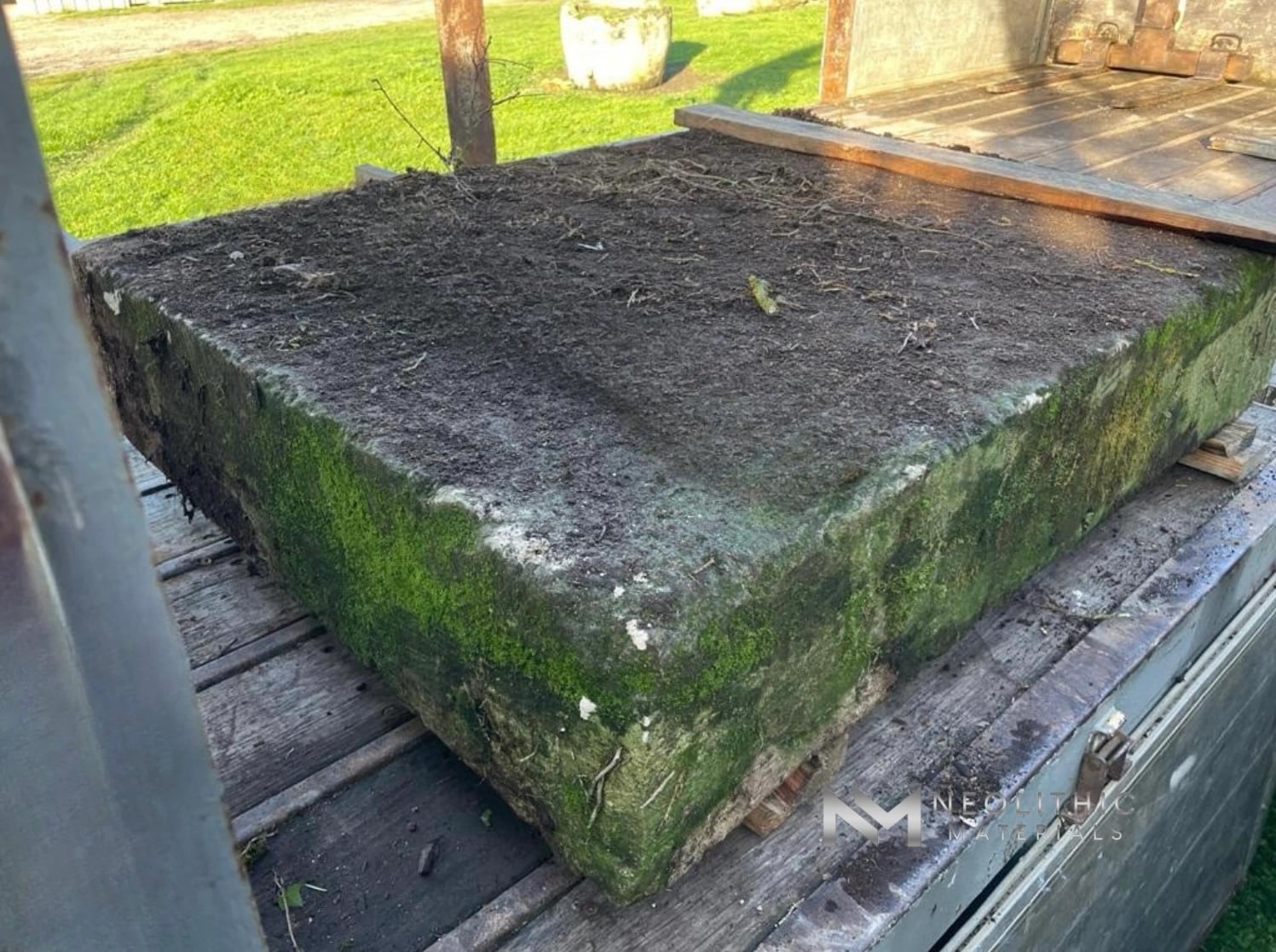 Tables and Slabs FI103-12 to 14.53x41x10: Low-perspective view looking down at a giant, thick natural stone architectural slab with rich organic moss and lichen growth coating its chiseled side profile, resting on a flat iron transport platform.