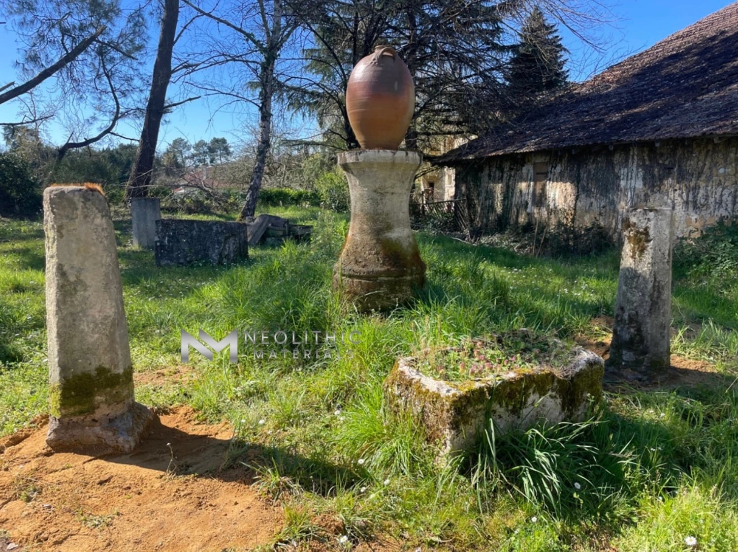 Miscellaneous FI103-16 & 17.13x43: Clear daytime capture of historic reclaimed stone posts and a matching baluster pedestal standing in a grassy field with an old tiled-roof barn under a blue sky backdrop.a