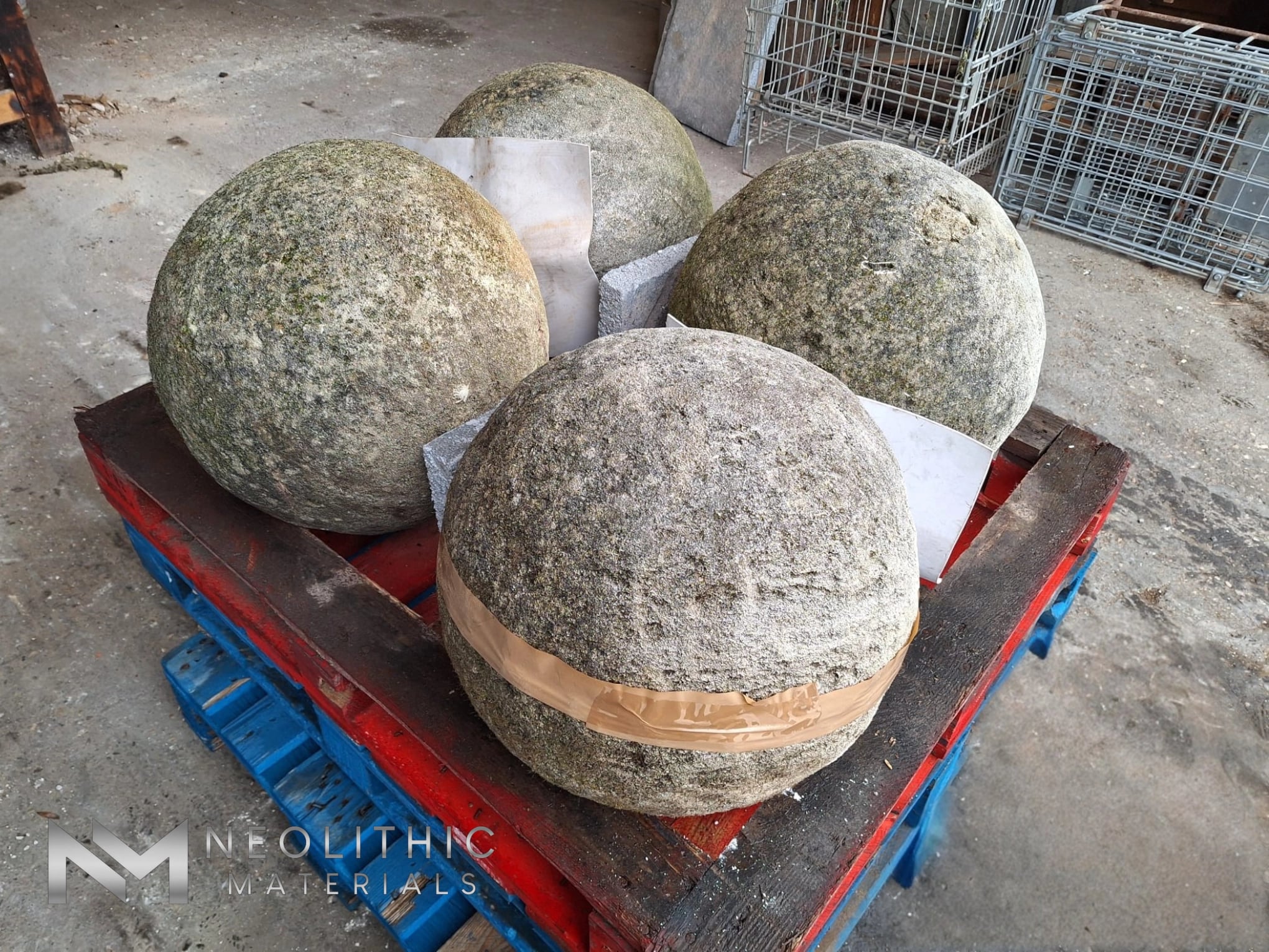 Miscellaneous FN101-01 to 04 - Cluster of four large rustic granite stone orbs wrapped in protective bands on a shipping pallet, captured from a high three-quarter angle inside a warehouse setting.