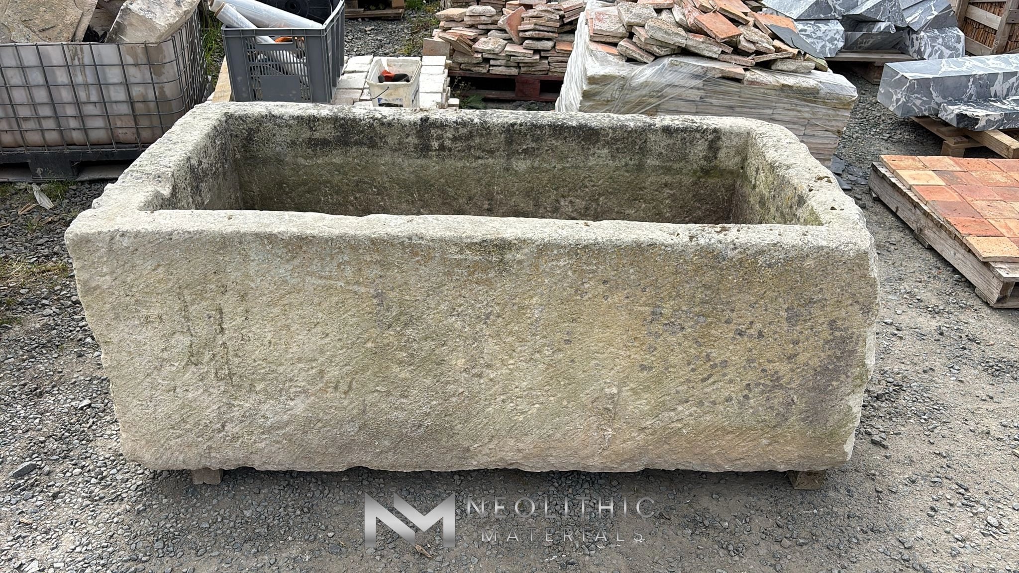 Trough FS101-05.EM elevated close-up view displaying a deep, weathered rectangular hand-carved stone basin, emphasizing its thick chiseled rims and rough limestone texture sitting on gravel ground.
