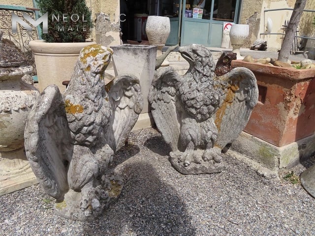 Miscellaneous FU101-07 & FU101-08: Ground-level exterior shot showcasing two hand-carved stone eagle garden sculptures with spread wings and aged, lichen-covered surfaces, displayed outside on a gravel courtyard with large ceramic planters in the background.
